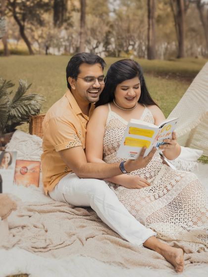 A duplicate of image 38, showing a happy couple reading together during their outdoor boho-themed maternity photoshoot.