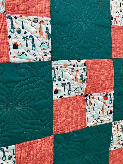 A close-up of the dinosaur quilt, showing the custom floral quilting in the solid blocks.