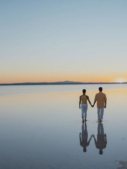 A beautiful silhouette of a couple walking hand-in-hand into the sunset on a Turkish salt flat. The reflection in the water and the vast, open sky create a feeling of infinite love and endless possibilities.