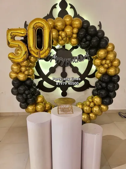 A grand 50th birthday celebration with a black and gold theme. This setup features a custom ship wheel backdrop, a balloon ring, and large '50' foil numbers.