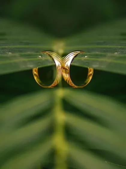 A creative and symmetrical reflection shot of a wedding ring placed on a green leaf. This unique composition connects the symbol of love with the beauty of nature.