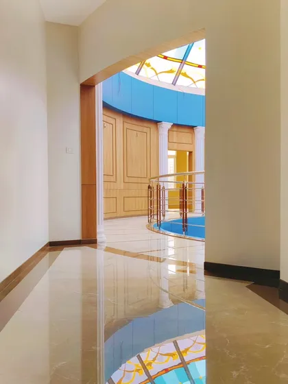 A view down the corridor leading into the clubhouse rotunda at Arihant Aspire. The reflection of the colorful dome on the polished floor creates a dynamic and ever-changing visual experience.