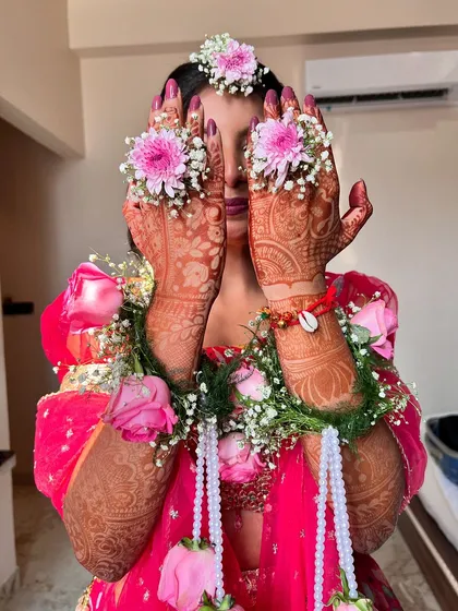 A playful shot of the bride hiding behind her floral jewelry. The intricate henna and the beautiful flowers are the stars of this Haldi look.