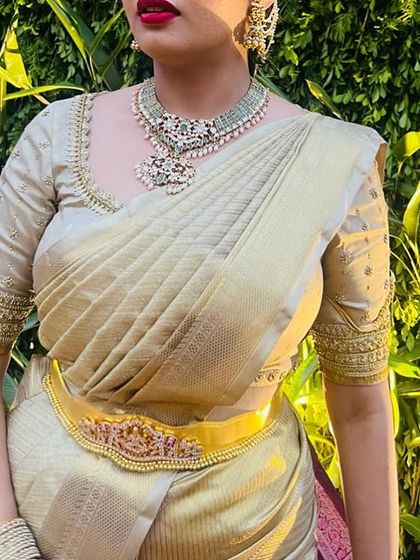 A close-up on the torso of a client wearing a gold Kanchivaram saree with a matching blouse featuring delicate embroidery on the sleeves.