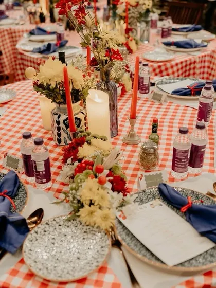 A beautifully set table for Aashvi and Akash's Italian-themed gala dinner. The red-and-white gingham tablecloth, rustic floral centerpieces, and custom menus were all designed to evoke the feeling of a long, joyful dinner in Italy.