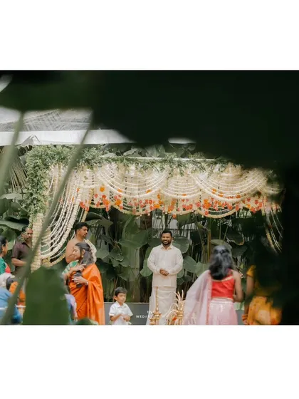 A candid moment of the groom at the mandap, with the lush green background peeking through the floral decorations.