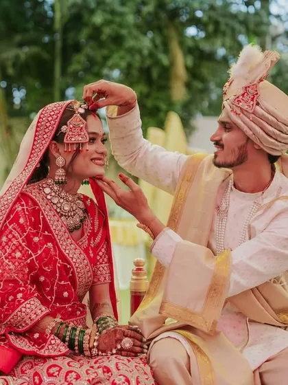 A sweet, candid moment where the groom adjusts an ornament on the bride's head during the wedding rituals.
