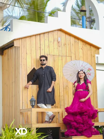 A creative and stylish shot of a couple posing with a paper umbrella against a rustic wooden cabin.