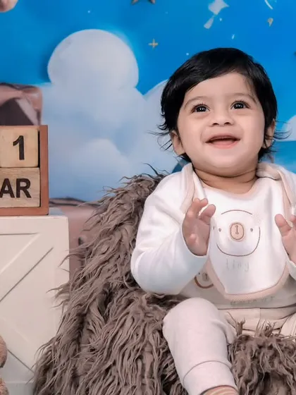 A close-up of a clapping, happy baby during her first birthday teddy bear photoshoot.