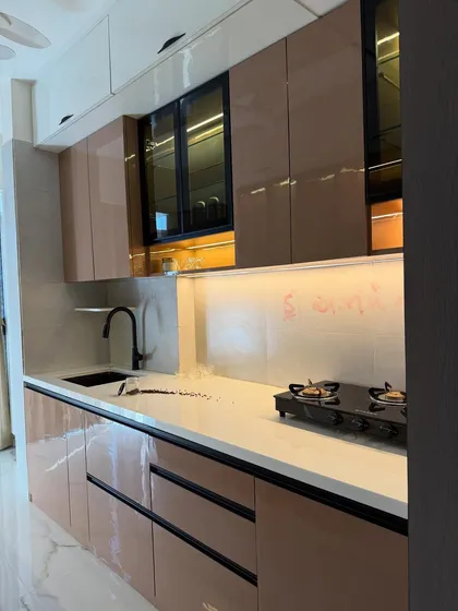 A beautiful parallel kitchen in rose gold and black, with glossy laminate finishes. The design includes glass-front upper cabinets and warm under-cabinet lighting.