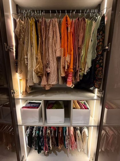 A stunning wardrobe with glass doors, where colorful garments are hung on display. Below, folded items are kept in neat bins.