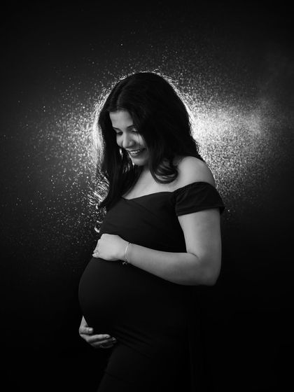 A magical black and white portrait with a halo of light. The backlighting creates a beautiful rim light around the mom-to-be's hair, giving her an angelic glow.