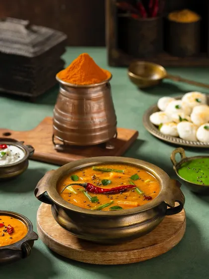 A South Indian sambar with idlis, styled with a copper pot of turmeric powder for a Rakesh Masala shoot.