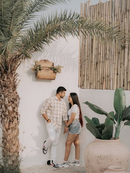 A relaxed portrait in a bohemian-style studio setting, with the couple posing against a wall with bamboo and palm tree accents.