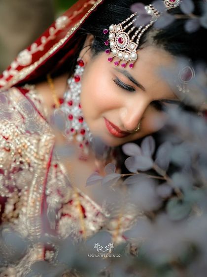 An artistic close-up of the bride, her face framed by soft leaves, highlighting her beautiful makeup and jewelry.