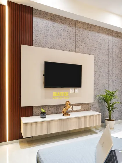 The TV unit in the Apex D'Rio parents' bedroom features a floating console with fluted cabinet fronts. The wall behind combines textured wallpaper with vertical wood-look louvers and integrated lighting for a dynamic effect.