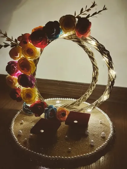 This is an engagement ring platter I designed for a client's special moment. It features two intertwined rings decorated with fairy lights and colourful paper flowers, creating a beautifully lit and romantic display for the exchange of rings.