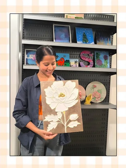 A student smiles as she displays her textured floral artwork, a white poppy created using sculpting paste in one of my mixed-media workshops.