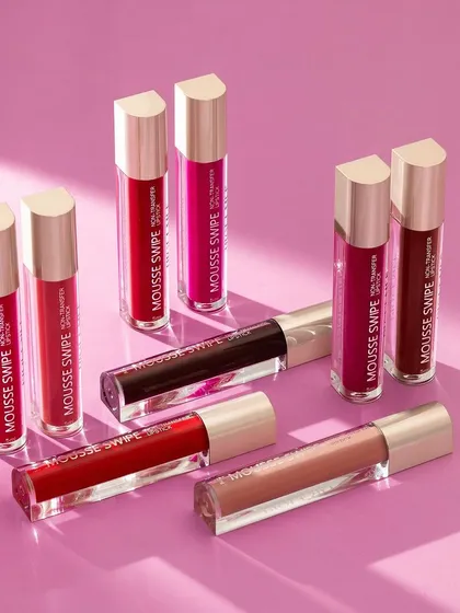 A group shot of liquid lipsticks arranged with clean lines and interesting shadows. The monochromatic pink background and hard light create a modern, chic aesthetic that focuses all attention on the products.