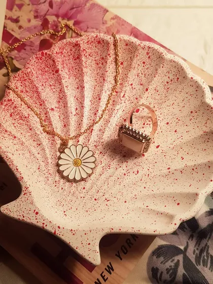 Our bestselling mini shell dish with a red speckled finish, styled with a daisy necklace and a book.