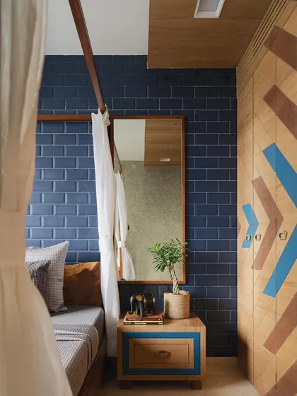 The guest room embraces a rustic aesthetic with a four-poster bed and an indigo brick-patterned wall. The wardrobe doors are cleverly camouflaged with a diagonal geometric pattern made from stained wood.