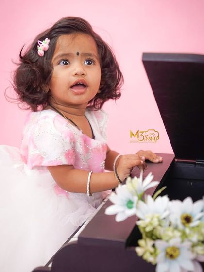 A little musician in the making. This toddler looks up with a curious expression while playing with a miniature piano prop against a soft pink backdrop.