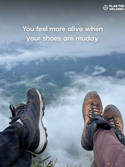 A close-up of muddy trekking shoes with a view of misty mountains. For us, feeling alive means getting your shoes muddy and embracing the raw beauty of nature.