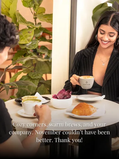 Cozy corners, warm brews, and your company. A couple enjoys a date at our cafe, surrounded by plants and soft light.