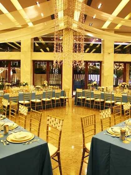 A wide view of a grand ballroom set for a private sit-down dinner. The combination of dramatic chandeliers and coordinated table settings demonstrates our capacity for large-scale, high-end events.