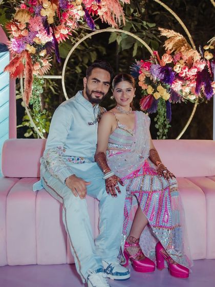 The couple seated against a vibrant floral backdrop.