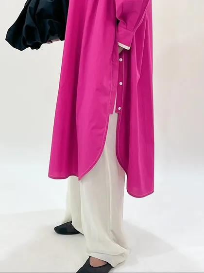 A detailed shot of the fuchsia longline shirt, showing its curved hem and button details.