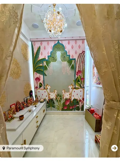 A stunning pooja room featuring a traditional Pichwai-style wallpaper with cows and lotus flowers. The white console and crystal chandelier add a touch of modern elegance.
