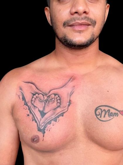A chest tattoo showing a baby's feet held in loving hands, forming a heart shape. This is next to a "Mom Dad" infinity tattoo, making it a beautiful family tribute.