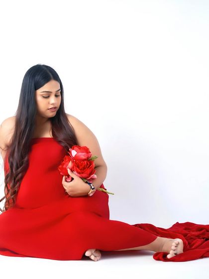 A quiet, seated portrait in a vibrant red gown, holding a bouquet of roses. This pose is perfect for a moment of calm reflection during your maternity session.