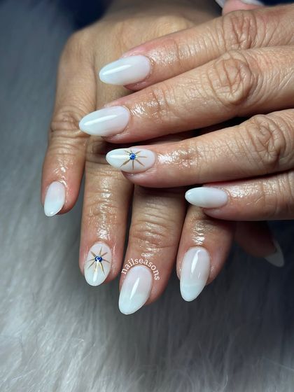 An elegant milky white manicure with a delicate, hand-painted evil eye starburst for a touch of protection and style.