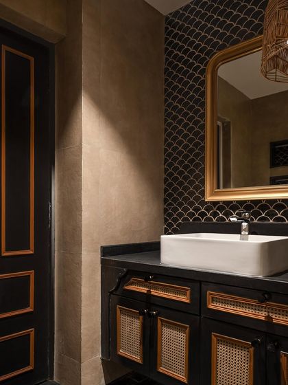 The powder room in our "Getaway to Galle" project features a custom black vanity with cane-fronted doors. The look is completed with a black fish-scale tile backsplash and a gold-framed mirror.