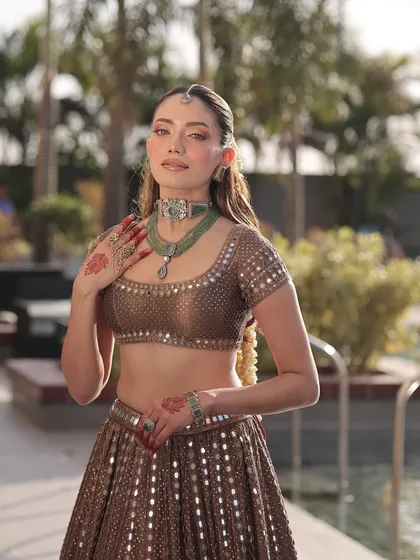 A timeless bridal look that combines tradition with a touch of modern sparkle. This bride looks radiant by the pool in a bronze mirror-work lehenga, paired with a beautiful green stone choker.