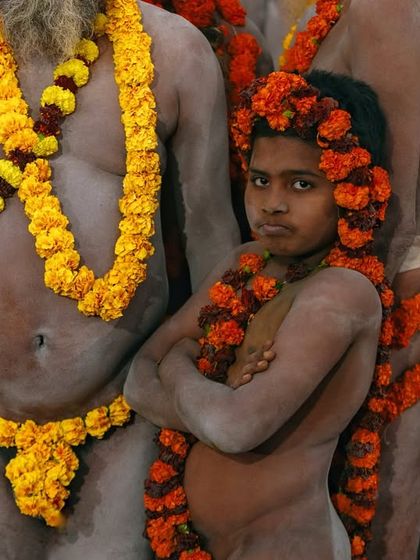 A young boy, initiated as a Naga sadhu, stands with his arms crossed, surrounded by adults. His serious expression shows the immense responsibility he is undertaking.