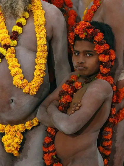 A young boy, initiated as a Naga sadhu, stands with his arms crossed, surrounded by adults. His serious expression shows the immense responsibility he is undertaking.