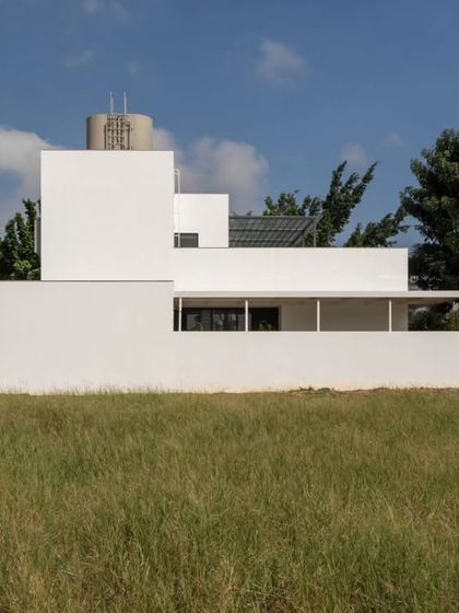The stark, minimalist form of the DUBEY Home's rear facade, set against a clear blue sky. This view emphasizes the building's simple geometric composition and clean, unadorned surfaces.