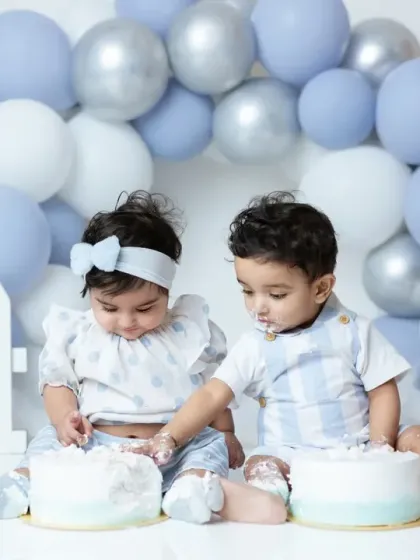 A fun and messy moment from a twin cake smash session. The siblings explore their first birthday cakes together in a coordinated blue and white setup.