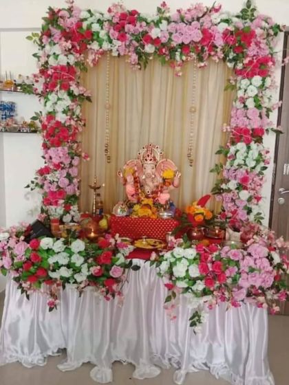 A beautiful heart-shaped arch made entirely of pink, red, and white roses. This design provides a soft and loving frame for the Ganpati idol, set against a simple cream curtain with delicate hanging bells.