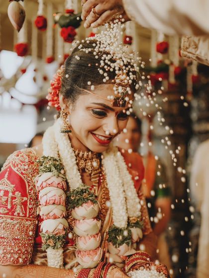 The bride's joyful smile as she is showered with Akshata rice during a key wedding ritual.