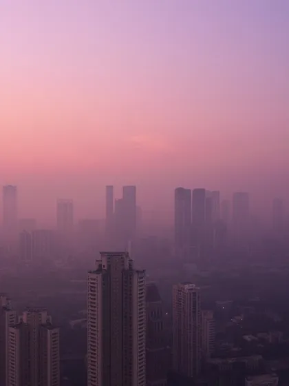 The upper portions of Mumbai's skyscrapers are silhouetted against a soft, hazy, purple and pink sky.
