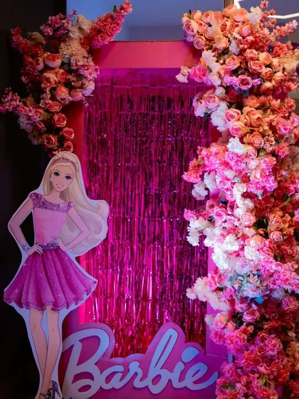 Come on Barbie, let's go party! This stunning photo booth features a life-sized Barbie cutout against a pink tinsel backdrop, framed by an extravagant pink and white floral arrangement.