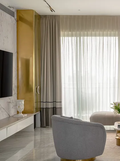 This view of the living room highlights the contrast between the cool marble TV wall and the warm brass of the custom storage unit. This play of materials adds depth and a touch of glamour to the space.