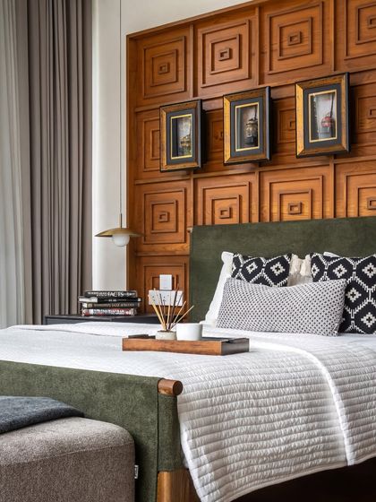 A different angle of the wood-paneled bedroom, showing the interplay of the green upholstered bed, patterned cushions, and the warm glow of the pendant light.