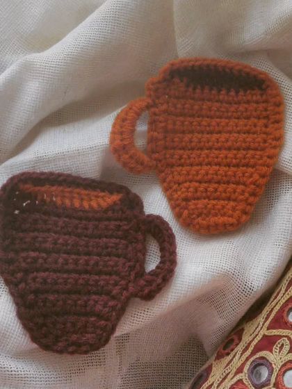 A pair of coffee mug-shaped coasters, perfect for your tea or coffee time. They make a cute and practical gift for the beverage lover in your life.