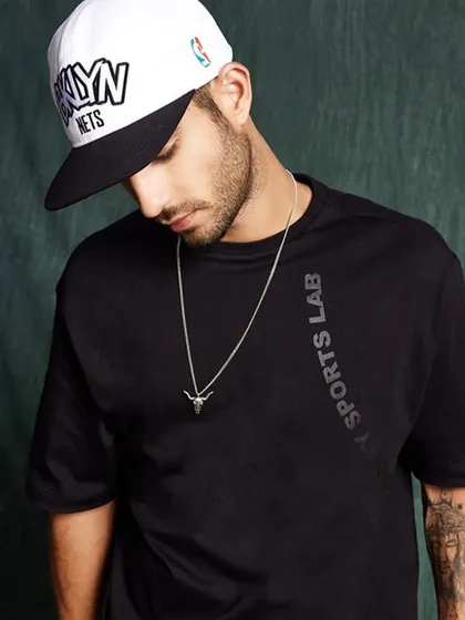 Styling for an athleisure collection. A black oversized tee is paired with a baseball cap and a simple silver chain for a clean, sporty, and modern look.