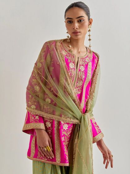 A bold and beautiful fuchsia and olive green suit. The contrast of the bright pink kurta with the earthy green dupatta, both tied together with gold embroidery, creates a striking and unique look.